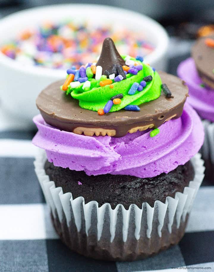 Chocolate cupcakes topped with orange frosting “brim,” black chocolate “hat,” and candy “broom” on a spooky plate